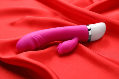 Photo of Pink vibrator on red fabric. Sex toy