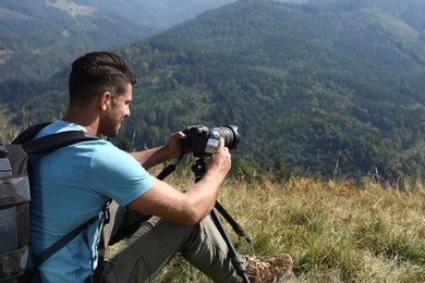 Photo of Man taking photo of mountain landscape with modern camera on tripod outdoors