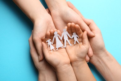 Photo of Parents and child holding paper cutout of family on light blue background, top view