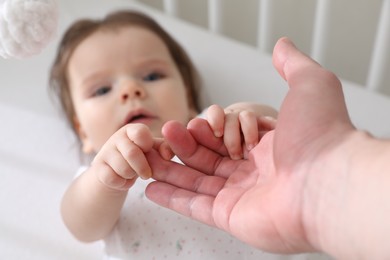 Photo of Father holding baby's hands in crib at home