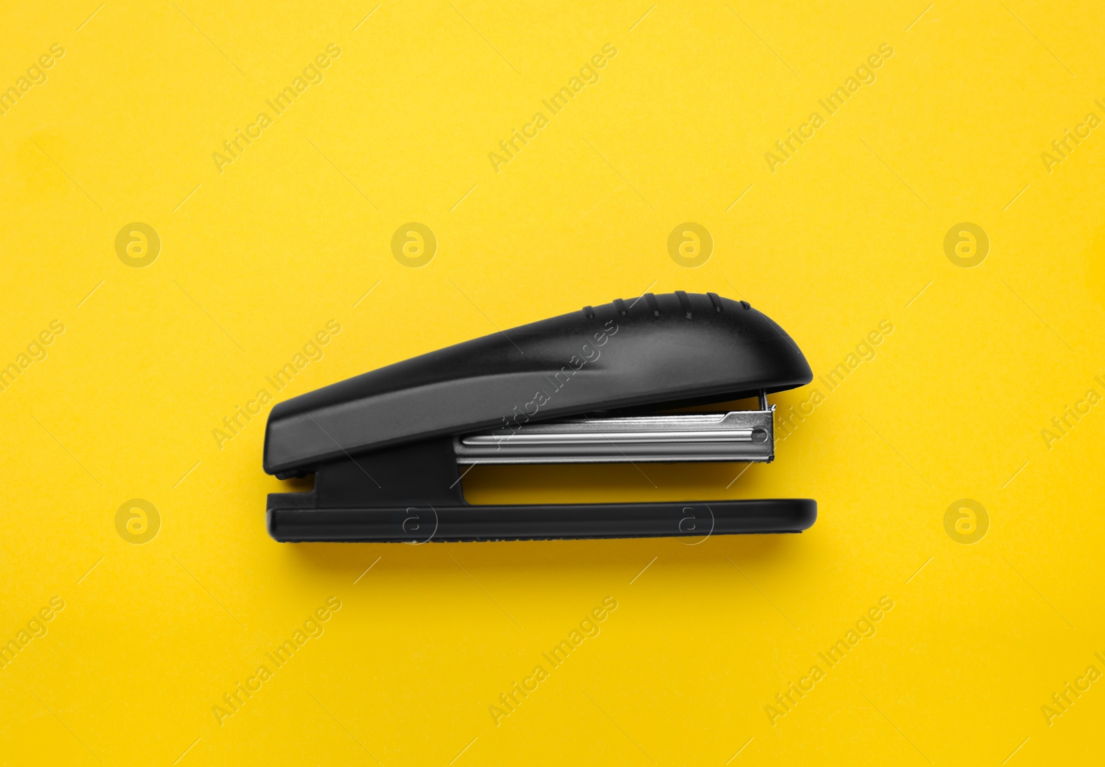 Photo of New bright stapler on yellow background, top view. School stationery