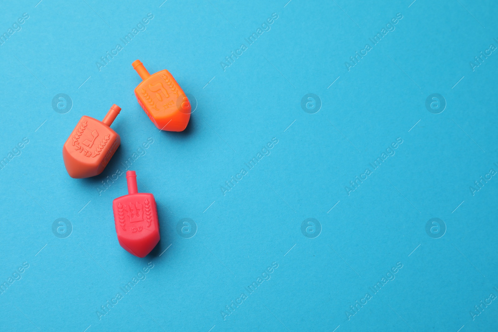 Photo of Colorful dreidels on light blue background, flat lay with space for text. Traditional Hanukkah game