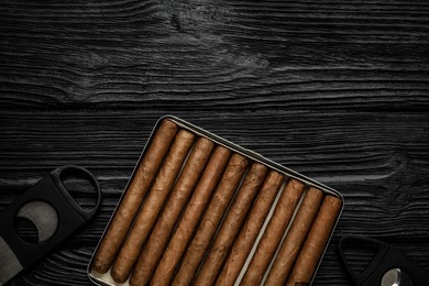 Photo of Cigars and guillotine cutters on black wooden table, flat lay. Space for text