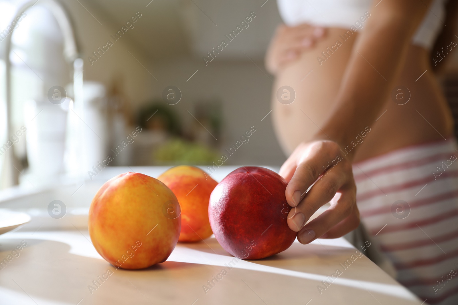 Photo of Young pregnant woman washing fresh sweet peaches in kitchen, closeup. Taking care of baby health