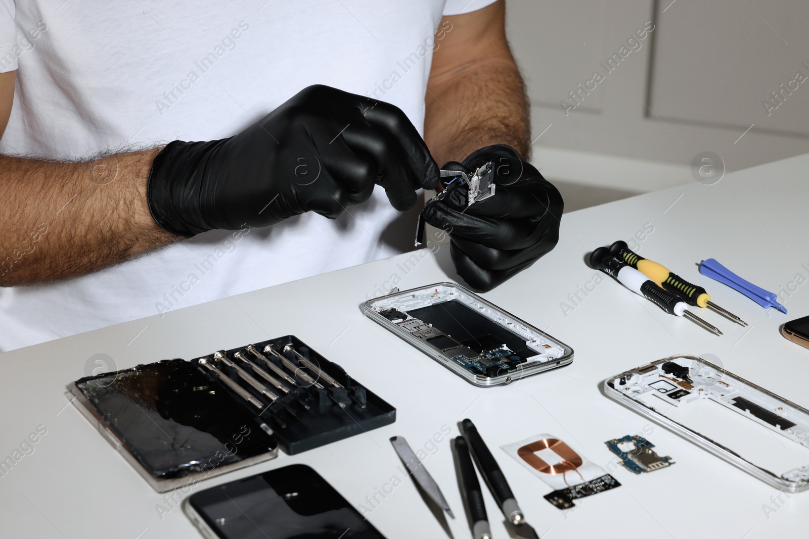 Photo of Technician repairing broken smartphone at white table, closeup