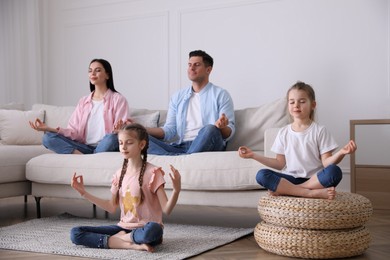 Family meditating in living room with comfortable sofa