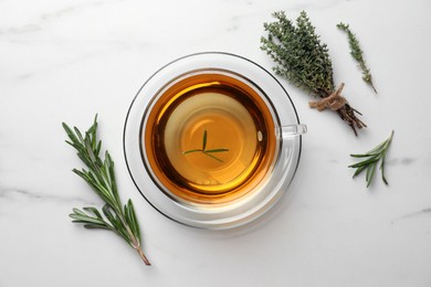 Photo of Cup of aromatic herbal tea with thyme and rosemary on white marble table, flat lay