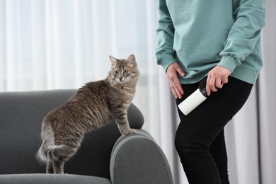 Photo of Pet shedding. Woman with lint roller removing cat`s hair from trousers at home, closeup