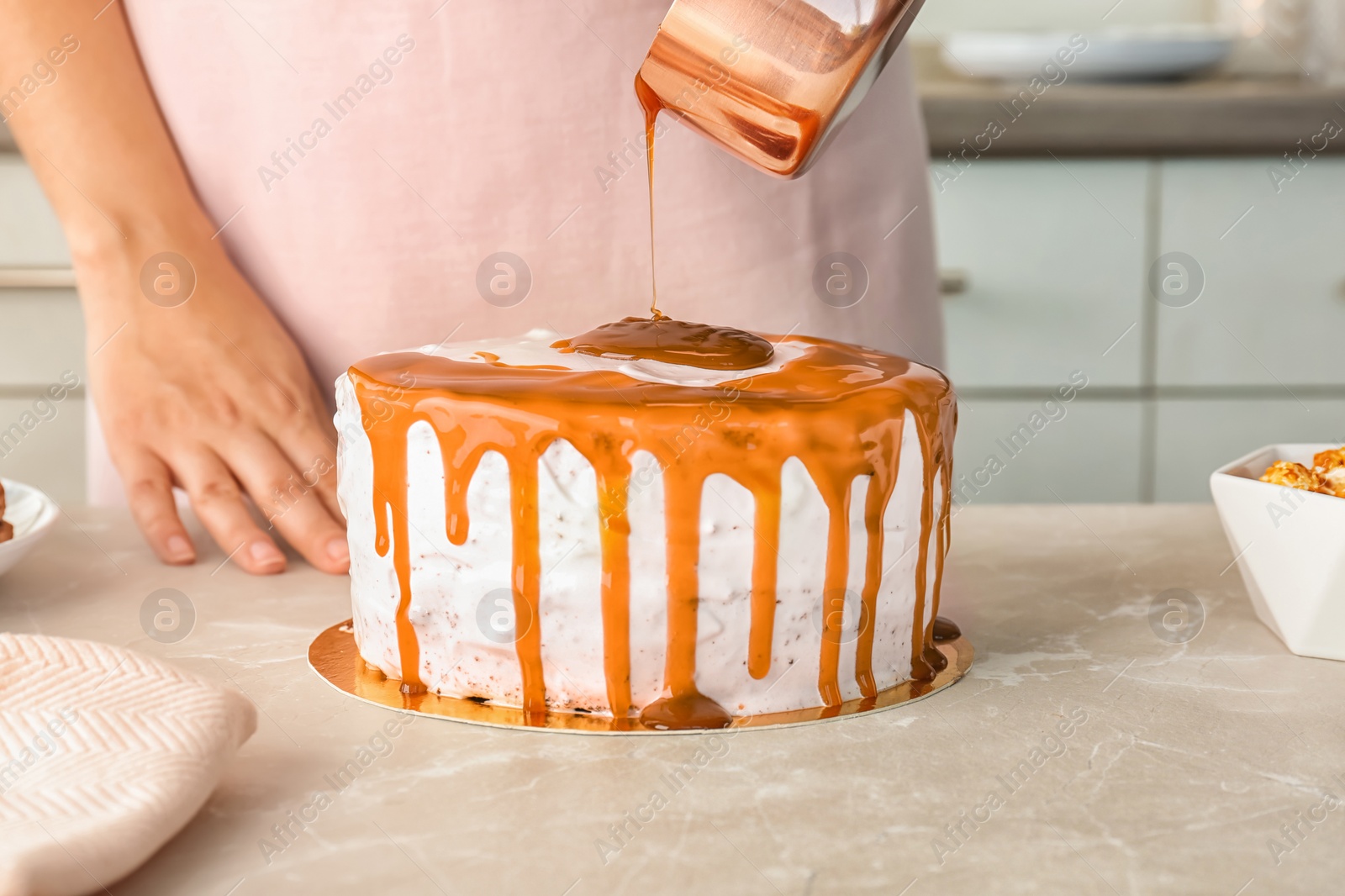 Photo of Young woman applying caramel sauce onto delicious homemade cake at table