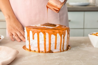 Young woman applying caramel sauce onto delicious homemade cake at table