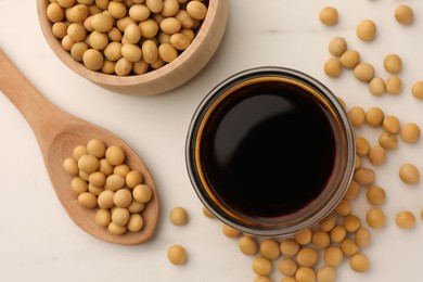 Soy sauce in bowl and soybeans on white table, flat lay