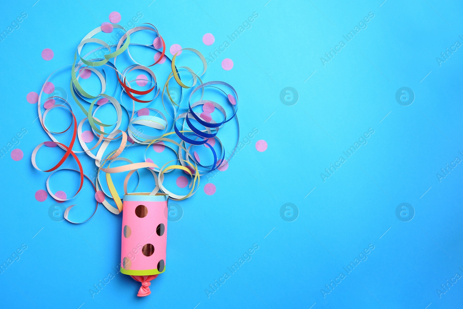 Photo of Beautiful serpentine and confetti bursting out of party popper on light blue background, flat lay. Space for text