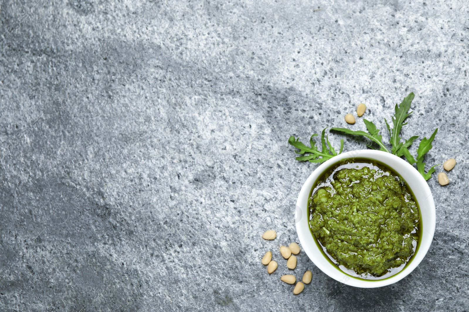 Photo of Bowl of tasty arugula pesto and ingredients on grey table, flat lay. Space for text