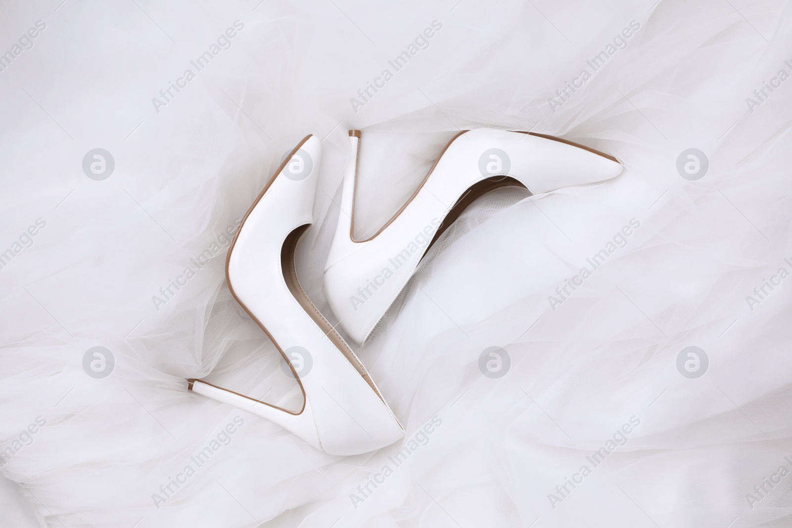 Photo of Pair of wedding high heel shoes on white veil, flat lay