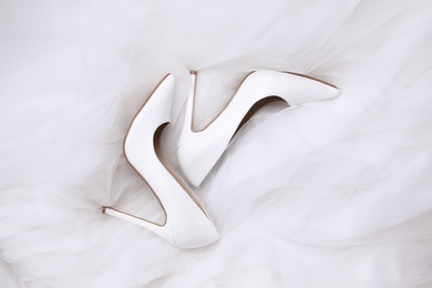 Pair of wedding high heel shoes on white veil, flat lay