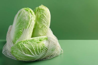 Fresh Chinese cabbages in string bag on green background, closeup. Space for text