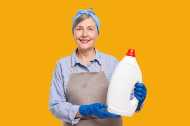 Happy housewife with bottle of detergent on orange background