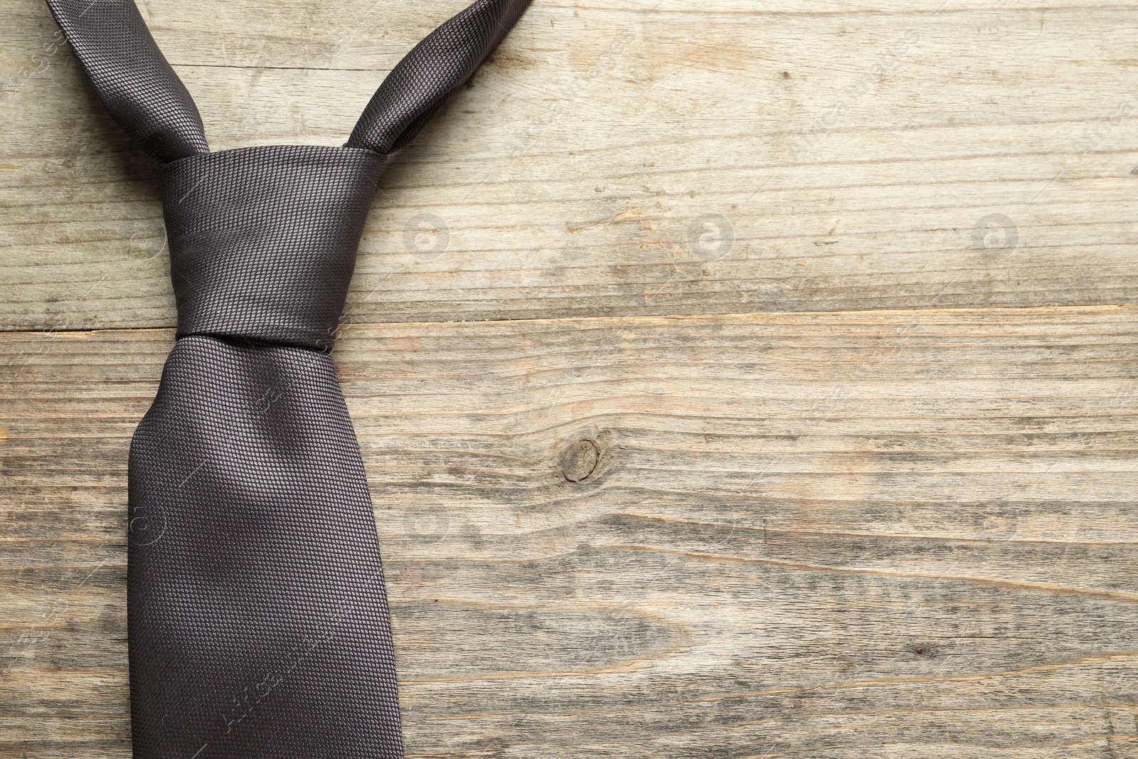 Photo of One necktie on light wooden table, top view. Space for text