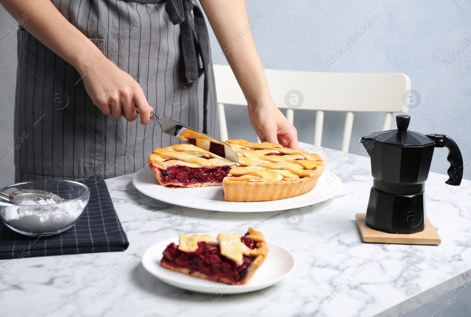 Photo of Woman cutting tasty cherry pie at white marble table, closeup