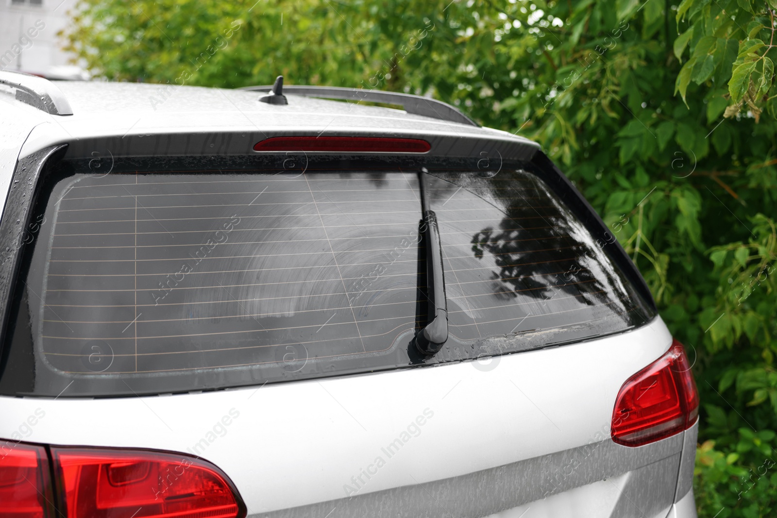 Photo of Wiper cleaning raindrops from car rear windshield outdoors