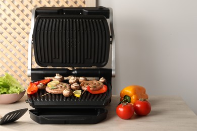 Photo of Electric grill with homemade sausages and vegetables on wooden table