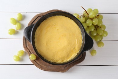 Photo of Fondue with tasty melted cheese and grapes on white wooden table, flat lay