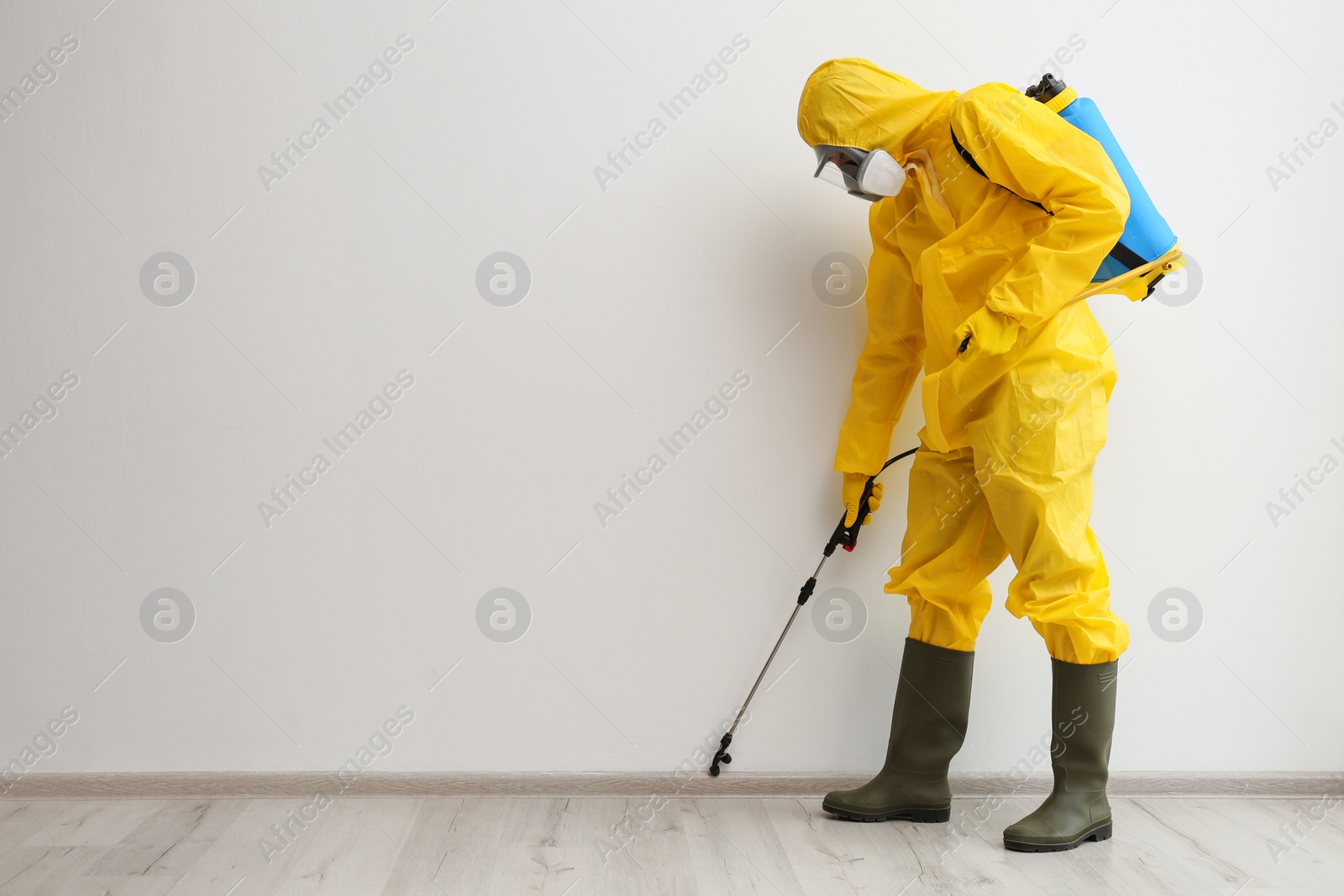 Photo of Pest control worker in protective suit spraying pesticide indoors. Space for text