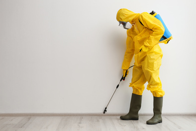 Pest control worker in protective suit spraying pesticide indoors. Space for text