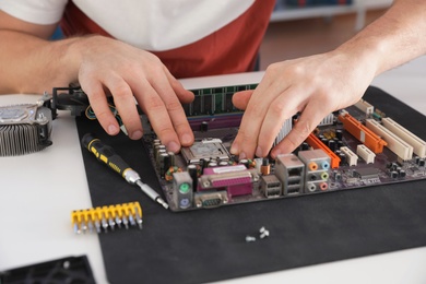 Male technician repairing motherboard at table, closeup