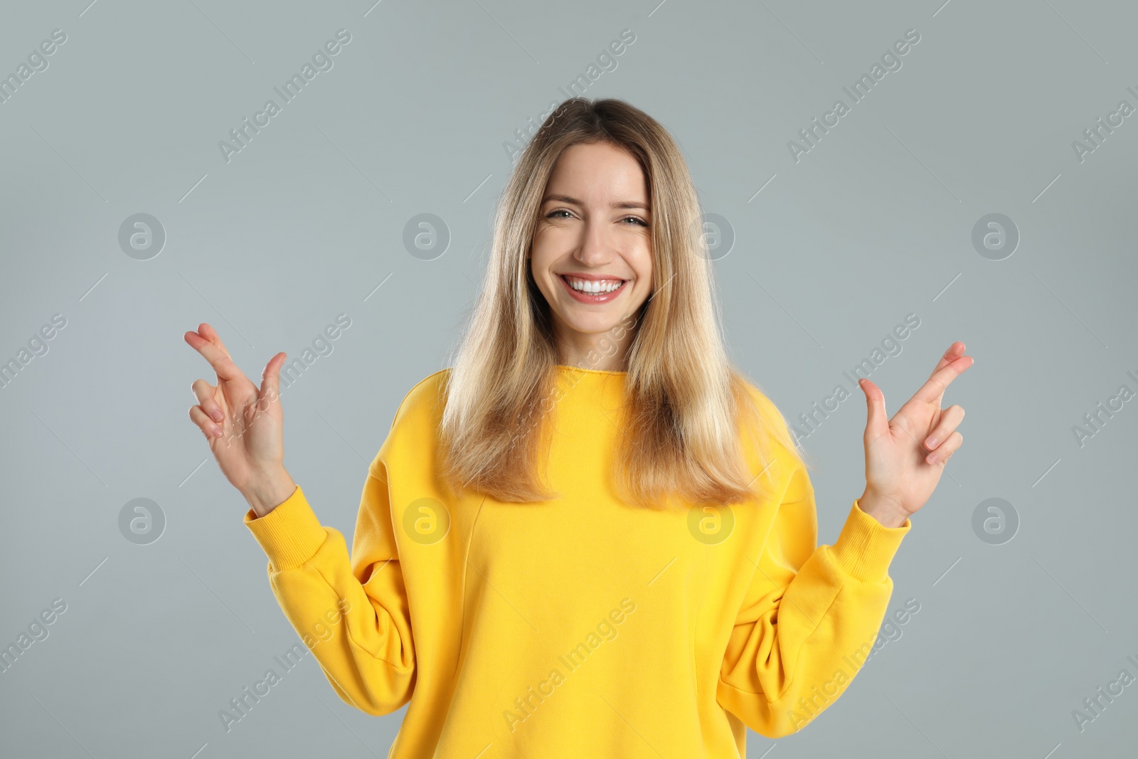 Photo of Woman with crossed fingers on light grey background. Superstition concept