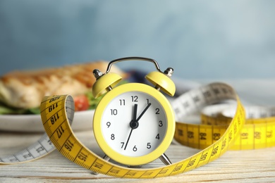 Photo of Alarm clock and measuring tape on white wooden table. Diet regime