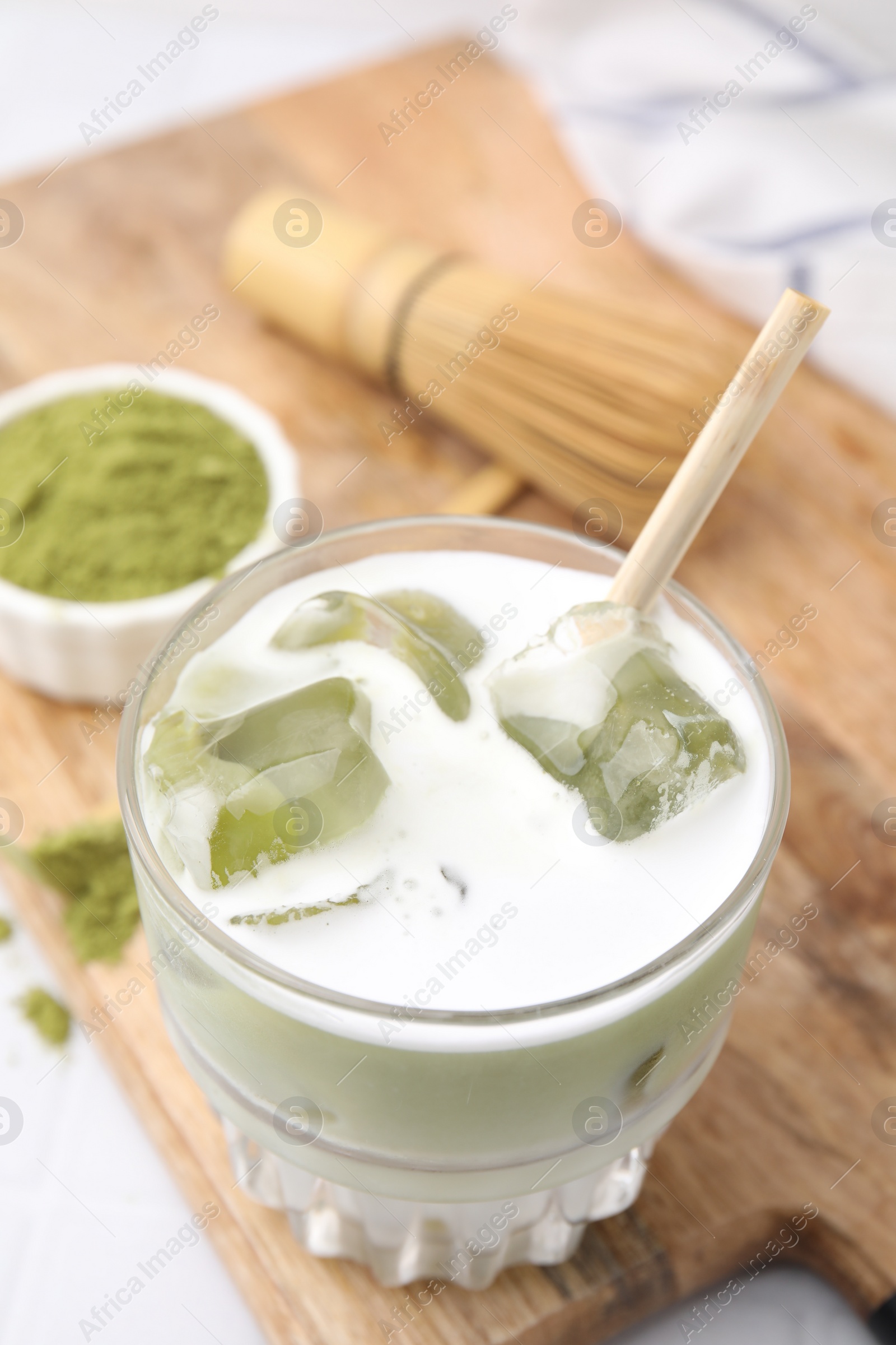 Photo of Glass of tasty iced matcha latte and powder on wooden board