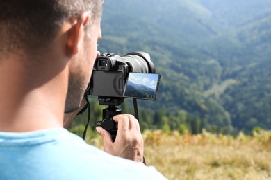 Photo of Man taking photo of nature with modern camera on stand outdoors