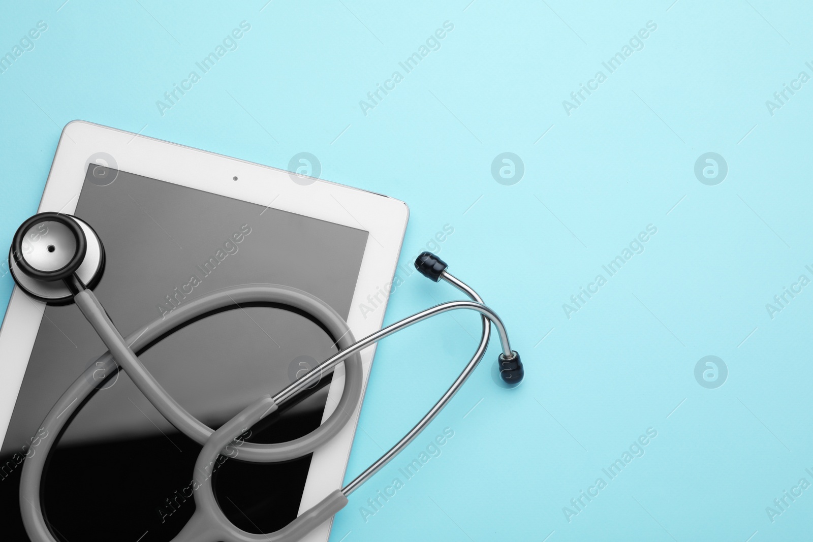 Photo of Computer tablet and stethoscope on turquoise background, top view. Space for text