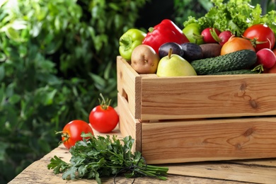 Photo of Crate full of different vegetables and fruits on wooden table outdoors, closeup. Harvesting time
