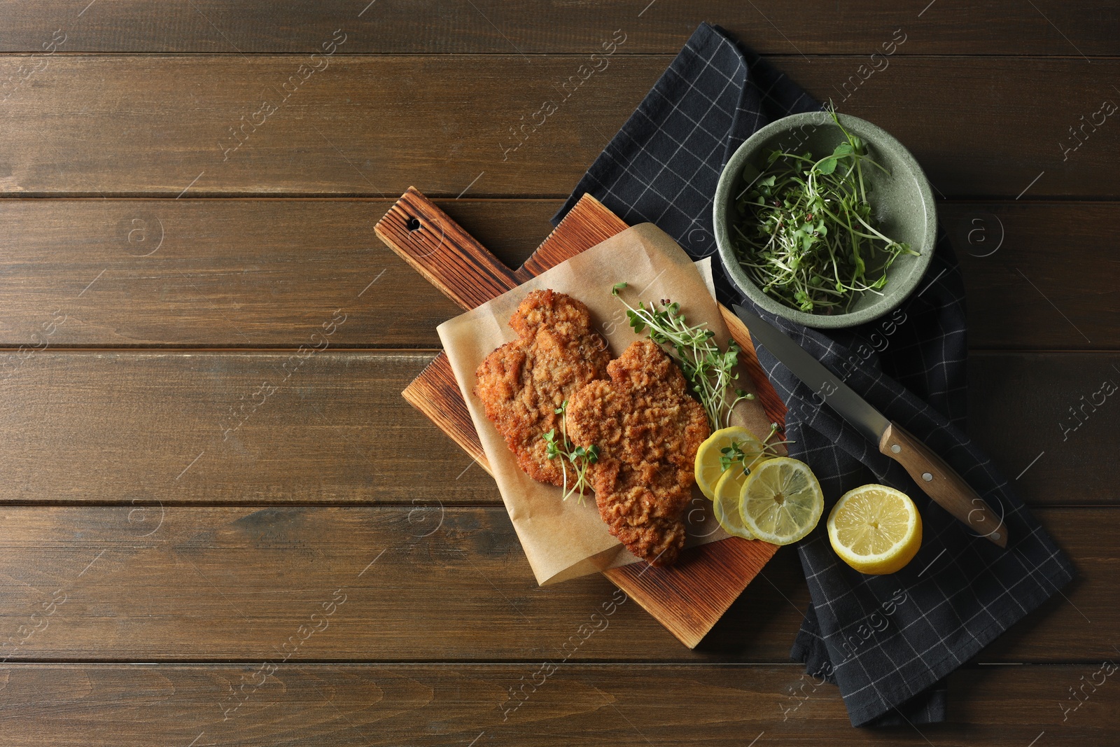 Photo of Tasty schnitzels served with lemon and microgreens on wooden table, flat lay. Space for text