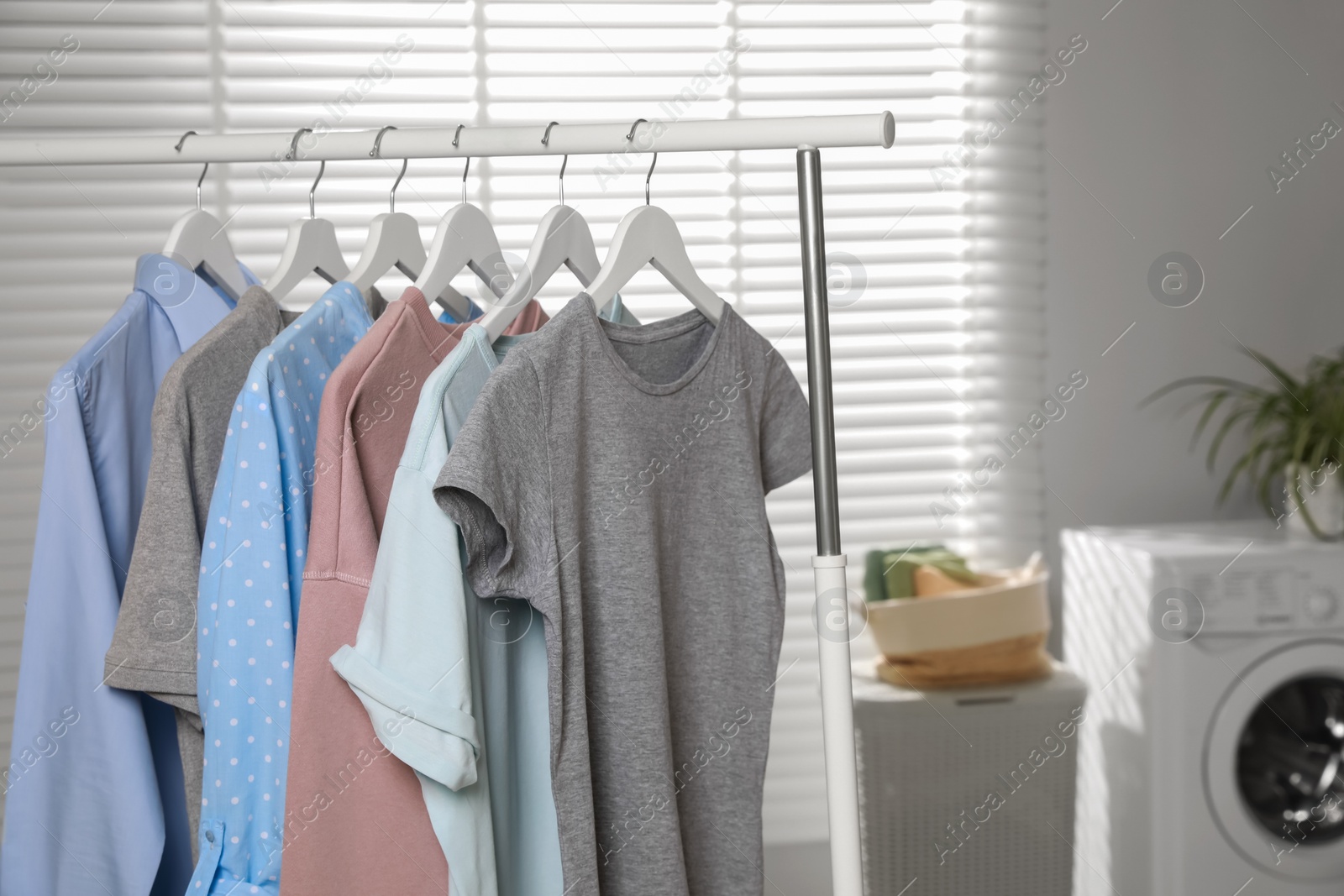 Photo of Different apparel hanging on clothes rack in bathroom, space for text