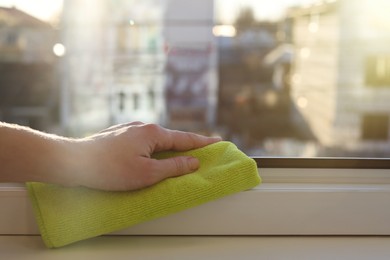 Photo of Woman cleaning window frame with rag at home, closeup