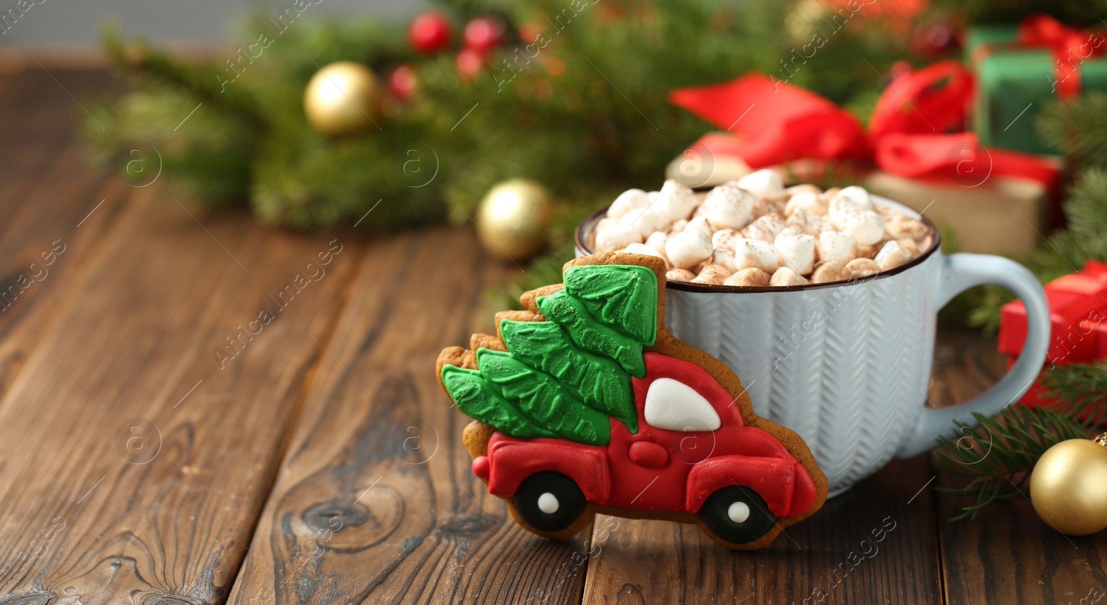 Photo of Tasty Christmas cookie in shape of car with fir tree, cocoa with marshmallows and festive decor on wooden table, closeup. Space for text