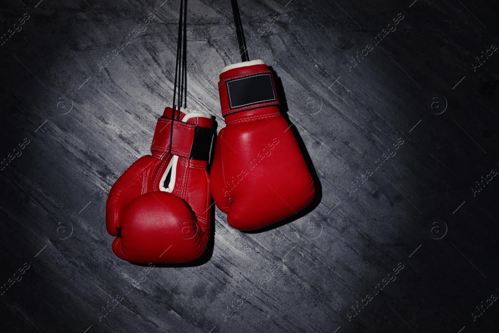 Photo of Pair of red boxing gloves hanging in spotlight on grey stone background. Space for text