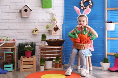 Adorable little girl with bunny ears and basket full of toy carrots in Easter photo zone