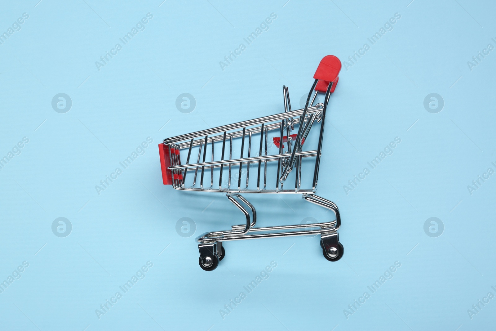Photo of Small metal shopping cart on light blue background, top view