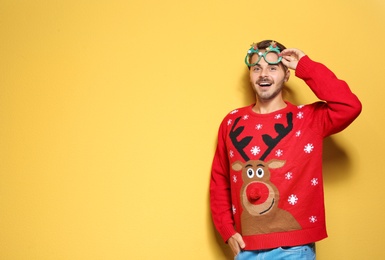 Young man in Christmas sweater with party glasses on color background. Space for text