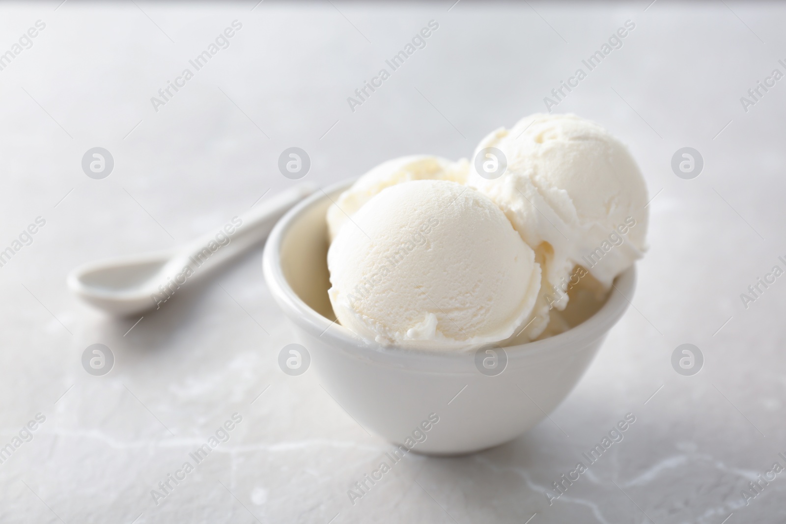 Photo of Bowl with tasty vanilla ice cream on light background