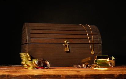Treasure chest, gold bars, coins, jewelry and gemstones on wooden table