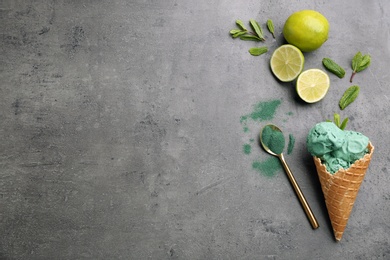 Photo of Flat lay composition with delicious spirulina ice cream cone and limes on grey background. Space for text