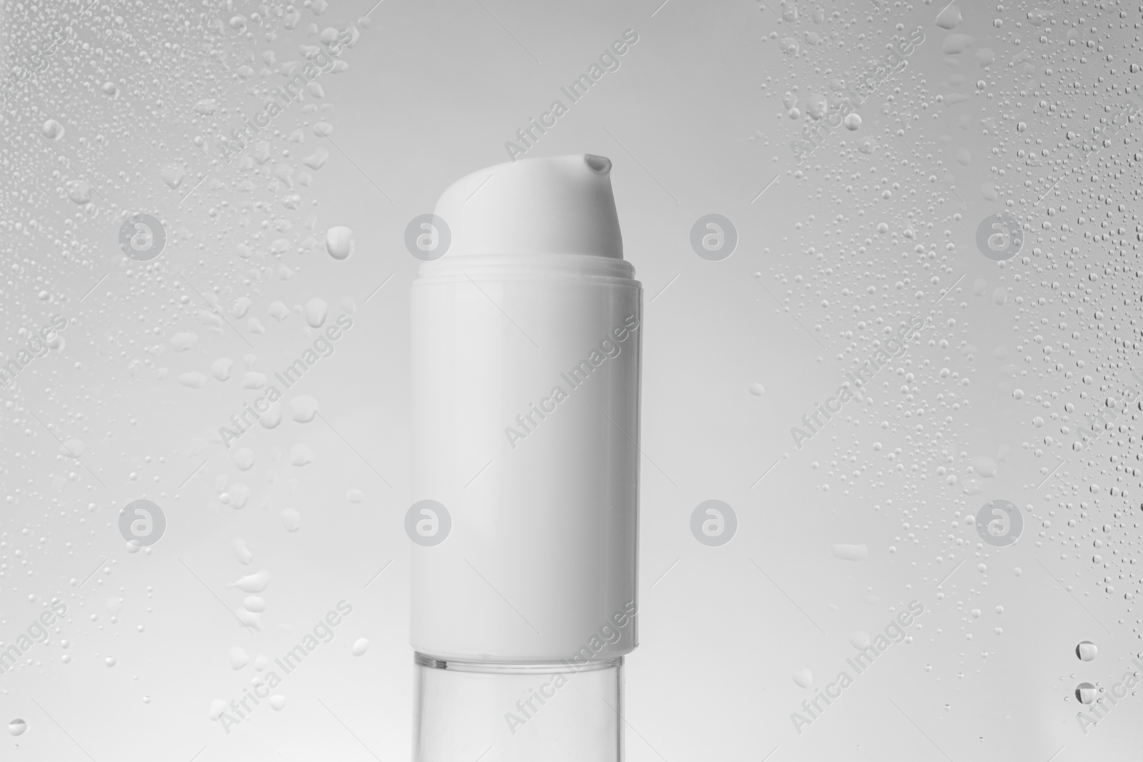 Photo of Bottle with moisturizing cream on grey background, view through wet glass