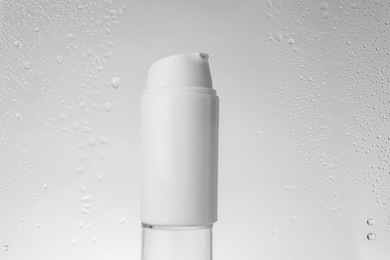 Photo of Bottle with moisturizing cream on grey background, view through wet glass