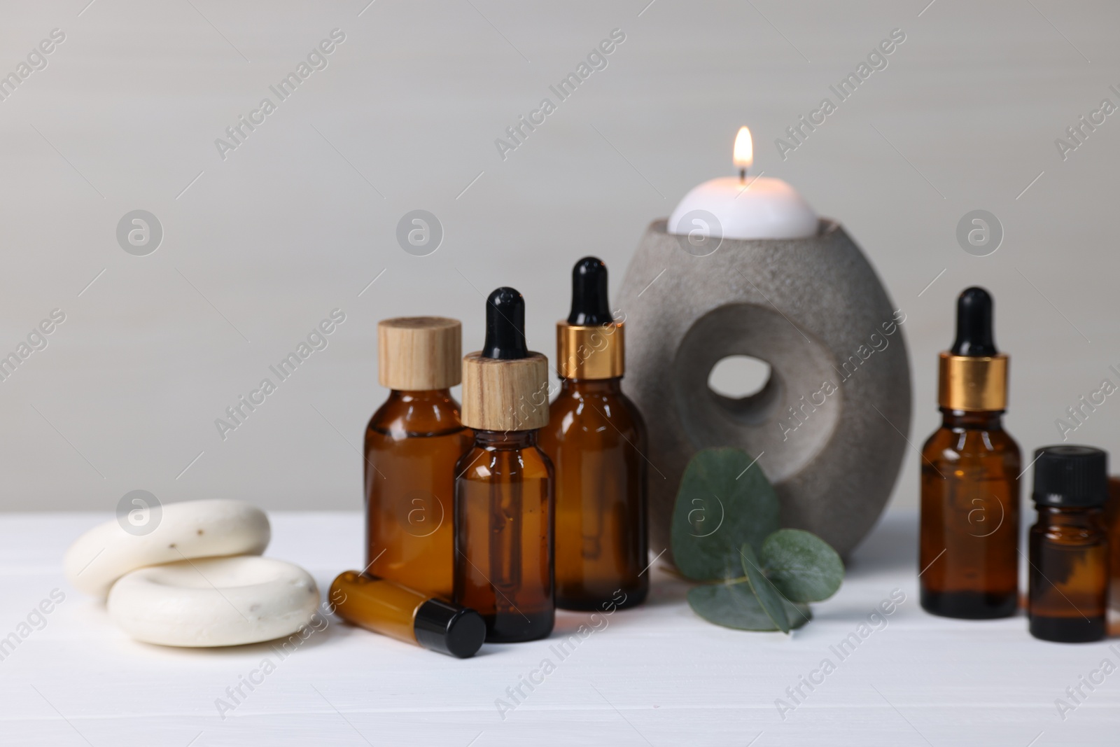 Photo of Different aromatherapy products, burning candle and eucalyptus leaves on white wooden table