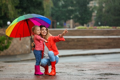 Photo of Happy mother and daughter with bright umbrella under rain outdoors